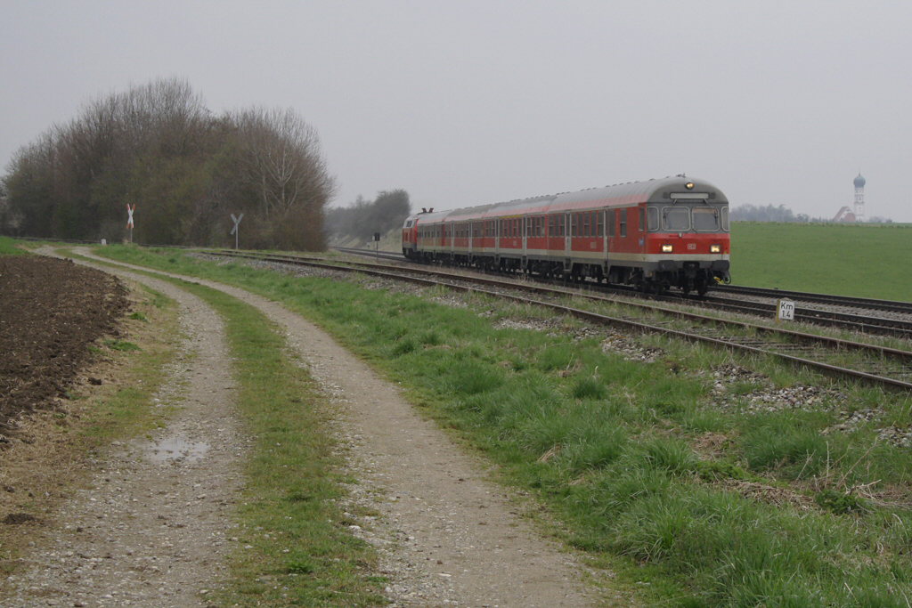 218 472-9 schiebt ihren RE von Kempten nach Mnchen, im Hintergrund ist die Pfarrkirche St. Johannes Baptist in Kaufering zu sehen, bei Epfenhausen, 14.04.12