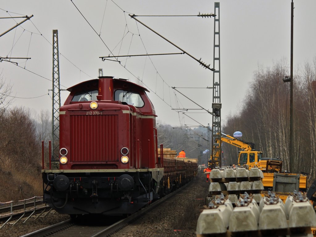 Am 03.03.2012 steht 212 370-1 der EfW-Verkehrsgesellschaft mit einem vollgeladenen Flachwagenzug mit Betonschwellen auf der KBS 480 bei Aachen Rothe Erde und wird von zwei Baggern entladen.