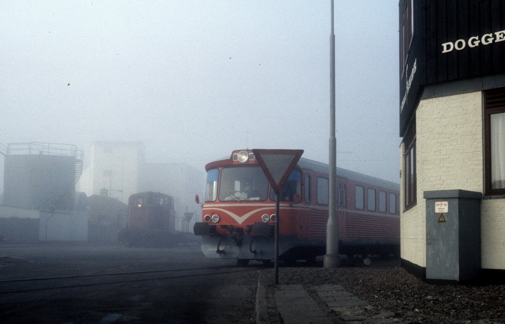 HP, Hjørring Privatbaner am 24. Februar 1975: Im Morgennebel fährt ein  Y-Zug , ein Triebzug bestehend aus einem Triebwagen (Ym) und einem Steuerwagen (Ys), zwischen dem Bahnhof und dem Hafen in Hirtshals in Nordjütland. - Im Hintergrund ahnt man eine Diesellok mit einigen Güterwagen.