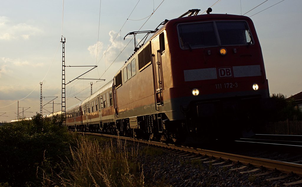 Im Gegenlicht der untergehenden Sonne führt 111 172-3 ihren Regionalzug von Rosenheim nach Freilassing. Bei Teisendorf legt sie sich am Abend des 10.07.2013 in die Kurve.