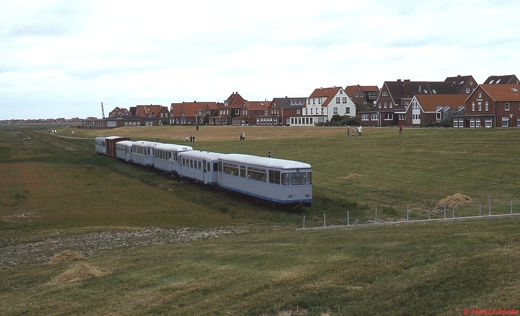 T 4 (ex Kreis Altenaer Eisenbahn) und T 2 (ex Euskirchener Kreisbahnen) der Inselbahn Juist passieren mit einem Zug voller ankommender Urlauber das Deichtor (Mai 1981). Der T 2 kam nach der Stilllegung zum DEV in Bruchhausen-Vilsen (dort T 44), während es den T 4 zu den Harzer Schmalspurbahnen verschlug, wo er als 187 013-8 im Einsatz steht.