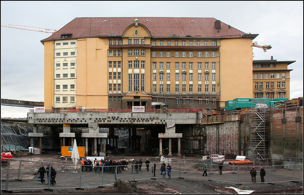 . Die schwebende Bahndirektion -

Im Bereich des zukünftigen nördlichen Gleisvorfeldes des neuen Stuttgarter Hauptbahnhofes wird das früherer Bahndirektionsgebäude aufwändig unterfahren. Das Gebäude wurde dazu zu einem Großteil auf Stützen gestellt.

Unter dieser Baugrube und auch dem Gebäude hindurch führen außerdem zwei neu gebauten Tunnelröhren für die Stadtbahn, die schon in Betrieb sind. Der alte Stadtbahntunnel war dem Bahntunnel im Weg.

Tage der offenen Baustelle, 05.01.2018 (M)
