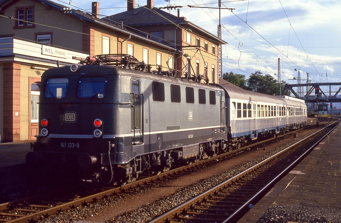 141 133, Weil am Rhein, 24.09.1987. Das Bahnhofsgebäude musste 1987 einer neuen Traase der Bundesstraße 3 weichen.
