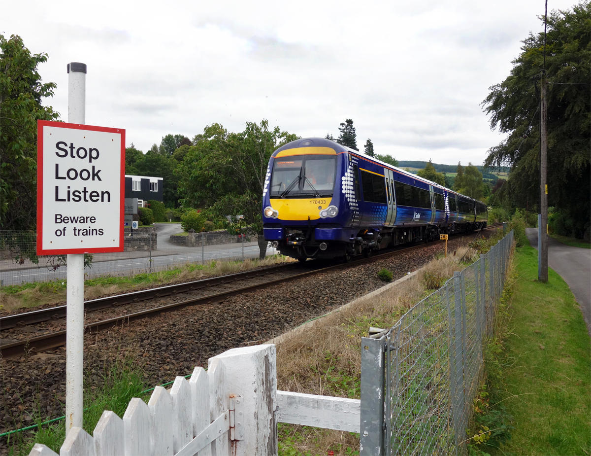 170 433 am 02.09.2014 auf der Highland Main Line (Perth-Inverness) von Perth kommend kurz vor dem Halt in Pitlochry. Pitlochry ist eines der Tore zu den Highlands und Zentrum für viele Wandertouren. Man beachte den Fußgängerübergang mit dem schnörkellosen Appell an den gesunden Menschenverstand.