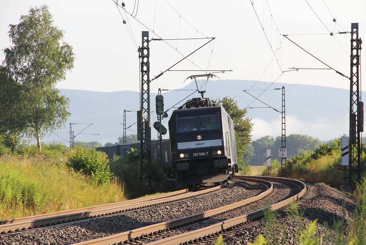 185 566-7 legt sich mit ihrem Containerzug in Richtung Süden kurz vor Wehretal-Reichensachsen in den Gleisbogen. Aufgenommen am 01.08.2013.