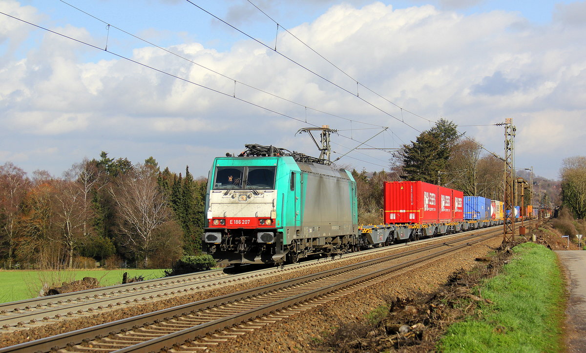 186 207 von der Rurtalbahn-Cargo kommt aus Richtung Aachen-West und fährt die Gemmenicher-Rampe hoch mit einem langen KLV-Containerzug aus Frankfurt-Höchstadt am Main(D) nach Genk-Goederen(B). 
Aufgenommen an der Montzenroute am Gemmenicher-Weg. 
Bei Sonne und Regenwolken am Mittag vom 8.3.2019.