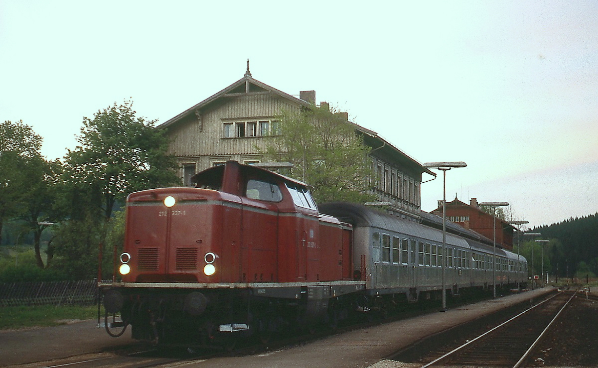 212 327-1 steht an einem Maiabend 1980 mit einem Nahverkehrszug abfahrbereit im Bahnhof Bayerisch Eisenstein, die mitten durch den Bahnhof verlaufende deutsch-tschechische Grenze ist im Hintergrund sichtbar