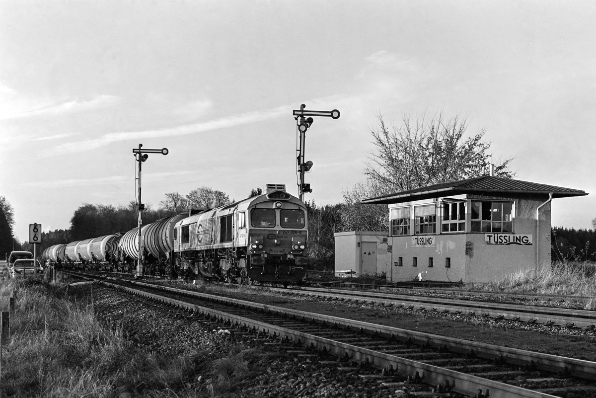 247 016-8 fährt mit ihrem Kesselwagenzug von Mühldorf nach Burghausen in den Bf Tüssling ein. Am 20.04.2016 ist das alte Stellwerk mit seinen Formsignalen noch in Betrieb. Diese werden noch im selben Jahr dem zweigleisigen Ausbau der Strecke Mühldorf - Tüssling weichen.
Analogaufnahme auf Ilford XP2 (400 ASA), Nikon F801, 25mm, 1/125s, f/11, Digitalaufnahme vom Negativ