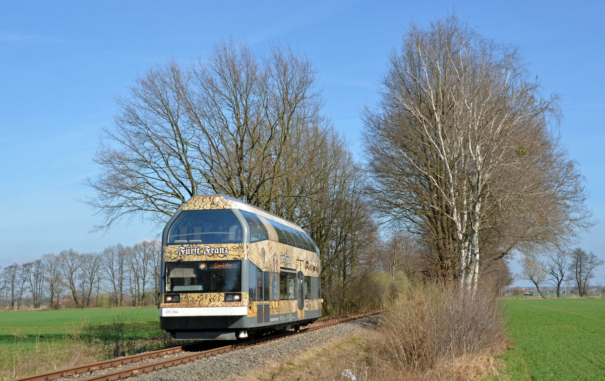 670 004 der DWE pendelte am 26.03.17 zum Saisonauftakt zwischen Wörlitz und Oranienbaum hin und her. Auf dem Weg nach Oranienbaum passiert Fürst Franz den BÜ zum örtlichen Klärwerk.