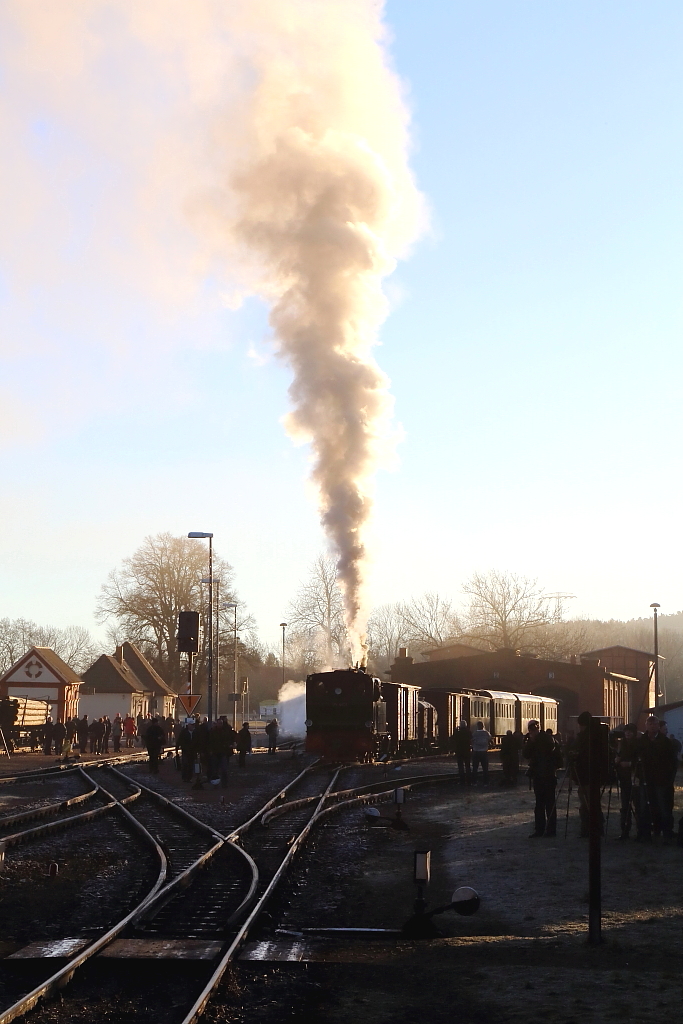 99 6101 am Morgen des 14.02.2015 auf Rangierfahrt im Bahnhof Gernrode. (Bild 8)
Hier hat sie die Güterwagen bereits mit den vor dem Lokschuppen stehenden Personenwagen vereinigt, wodurch der Zug nun komplett ist und nur noch am Bahnsteig bereitgestellt zu werden braucht. Wie man sieht, sind die Fahrgäste mittlerweile zahlreich eingetroffen. Faszinierend fand ich hier auch die bei absoluter Windstille im Gegenlicht aufsteigende Dampffahne.