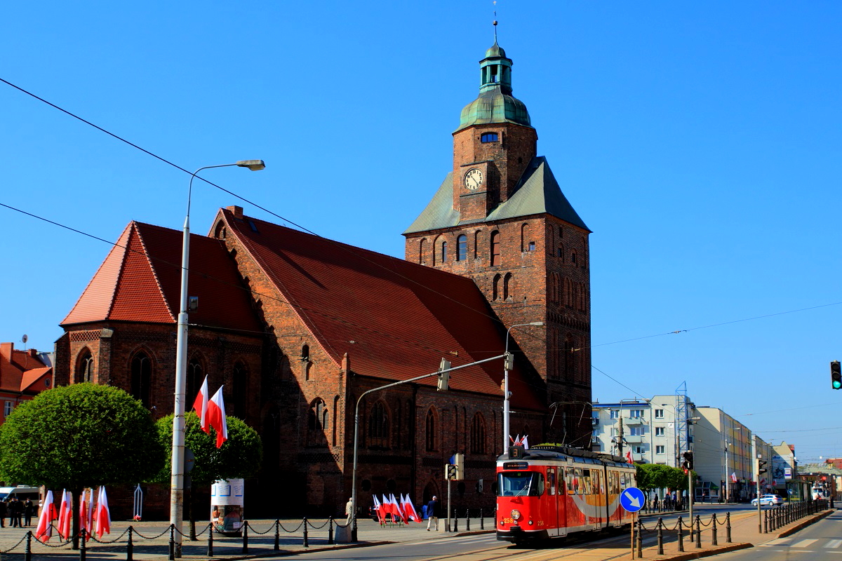 Am 03.05.2016 verläßt der Tw 258 (ex Kassel 305) die Haltestelle Katedra in Richtung Walczaka. Im Hintergrund der Dom St. Marien aus dem späten 13. Jahrhundert. Wegen des Feiertages (Verfassungstag) sind die Straßen fahnengeschmückt.