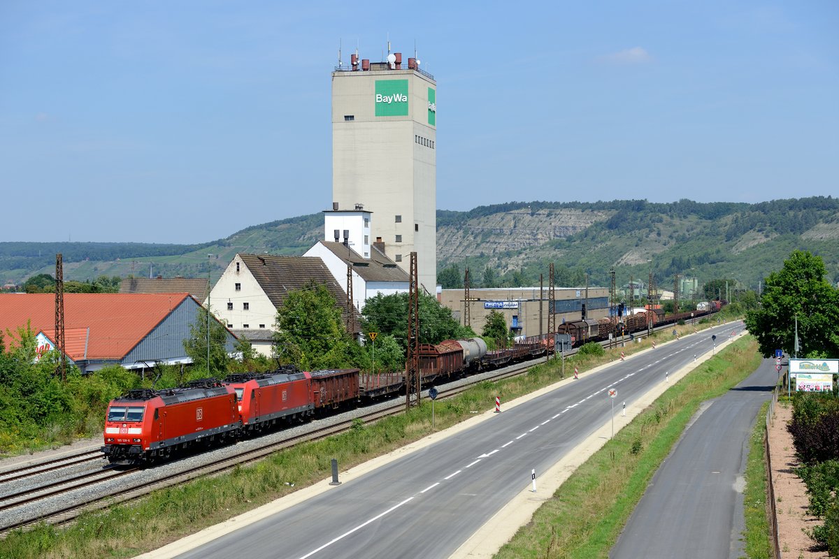 Am 18. Juli 2014 passierte eine Doppeltraktion, bestehend aus den Schweiz-tauglichen 185 126 und 138, mit einem langen EZ 51887 von Mannheim Rbf nach Nürnberg Rbf das markante BayWa Lagerhaus und die Baumschule Müllerklein in Karlstadt.