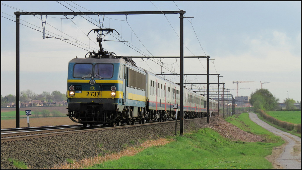 Am frühen Abend des 21.April 2016 ist die belgische 2737 mit einen Regionalzug nach Hasselt unterwegs. Hier zu sehen unweit von Tongeren (B).