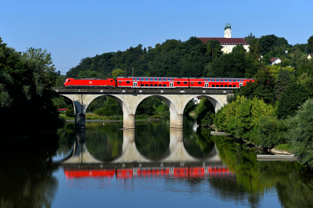 Am Morgen des 14. Juli 2018 floss die Vils ruhig dahin, als sie 146 240 mit ihrem RE 4056 nach Passau bei Vilshofen überquerte. Im Hintergrund ist die Benediktiner-Abtei Schweickelberg zu sehen. 