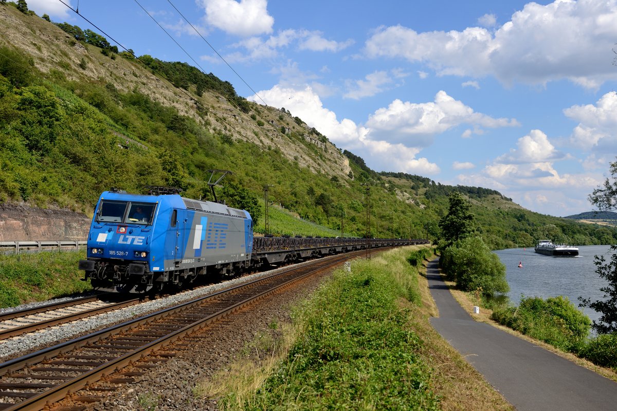 Am Nachmittag des 02. Juli 2014 kam die LTE 185 528 mit dem Kupferanoden-Zug von Pirdop in Bulgarien nach Olen in Belgien durch das Maintal gefahren. Bei Kilometer 28.2 zwischen Karlstadt und Gambach gelang diese Aufnahme mit stromaufwärts fahrendem Schiff.