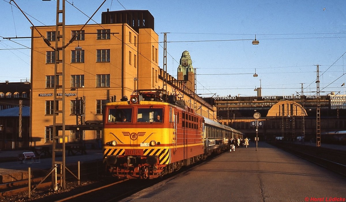 An einem Maiabend 1988 steht Sr1 3064 mit einem Nachtschnellzug abfahrbereit im Bahnhof Helsinki. Die Sr1 war zum damaligen Zeitpunkt die einzige finnische E-Lok-Baureihe. Die 140 bzw. 160 km/h schnellen Maschinen mit einer Dauerleistung von 3.100 kW wurden zwischen 1973 und 1984 in der Sowjetunion gebaut, die elektrische Ausrstung lieferte ABB.