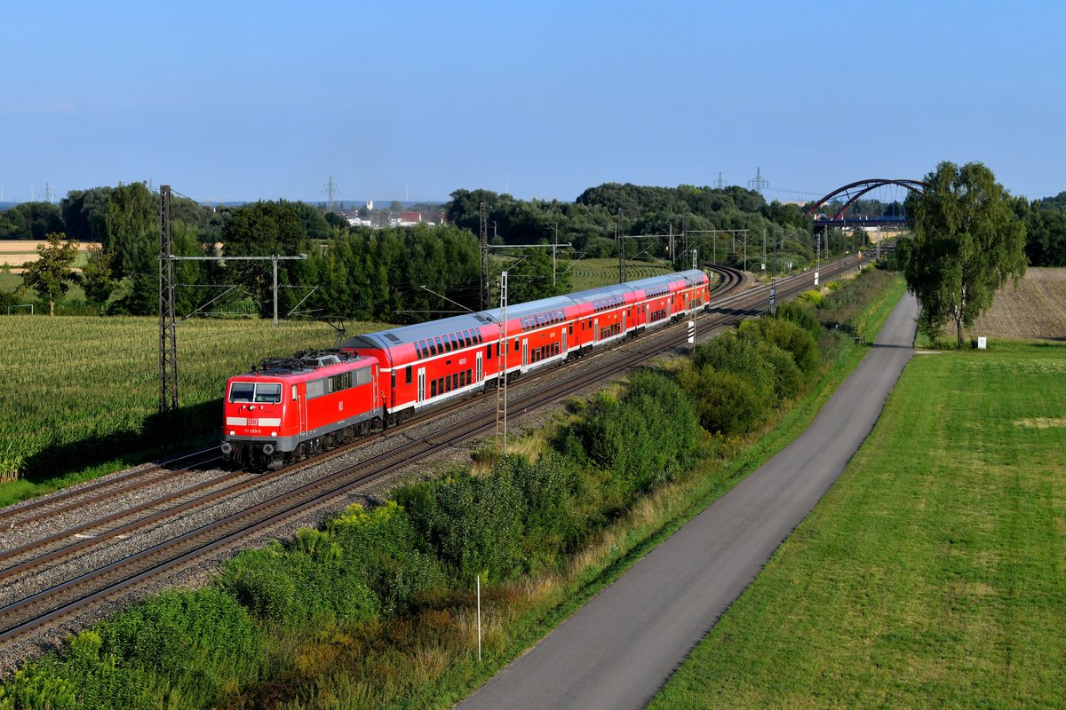 Auch auf der KBS 910 läuft die Zeit der Einsätze der Baureihe 111 unweigerlich ab. Der Wechsel auf die neuen Triebwagen der Baureihe 445 ist praktisch abgeschlossen. Am 26. Juli 2018 war 111 055 noch vor der RE 57096 zu beobachten, einem Verstärker zwischen München und Donauwörth zur Berufsverkehrszeit. Die Aufnahme entstand bei Nordheim. 