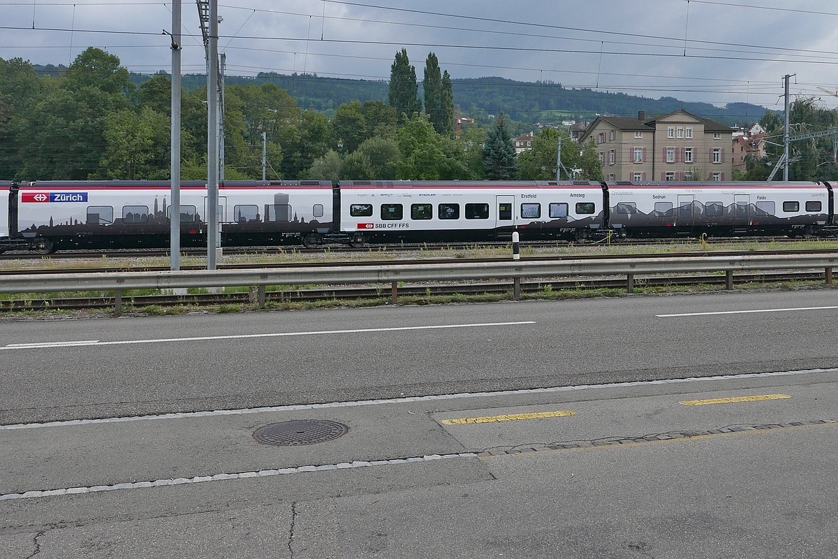 Auf Wagen 4 von RABe 501 004-2 ist die Skyline von Zürich und auf Wagen 5 folgt die Silhouette der Vorläufer des Gotthardmassivs sowie die Orte Erstfeld und Amsteg am bzw. über dem Gotthard-Basistunnel. Aufnahme entstand in Rorschach am 24.08.2018.

Die jeweilige Beklebung der Einzelwagen hat bereits Herbert fotografiert und hier hochgeladen.