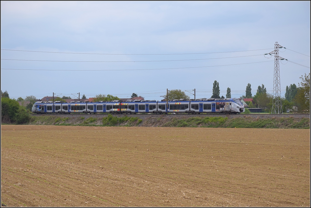 Bahn im Elsass. Einer der neuen Alstom Coradia Polyvalent Triebzge fhrt an Raedersheim vorbei. Es handelt sich um den Vorortzug B 83515 mit Zweikraftantrieb. April 2017.