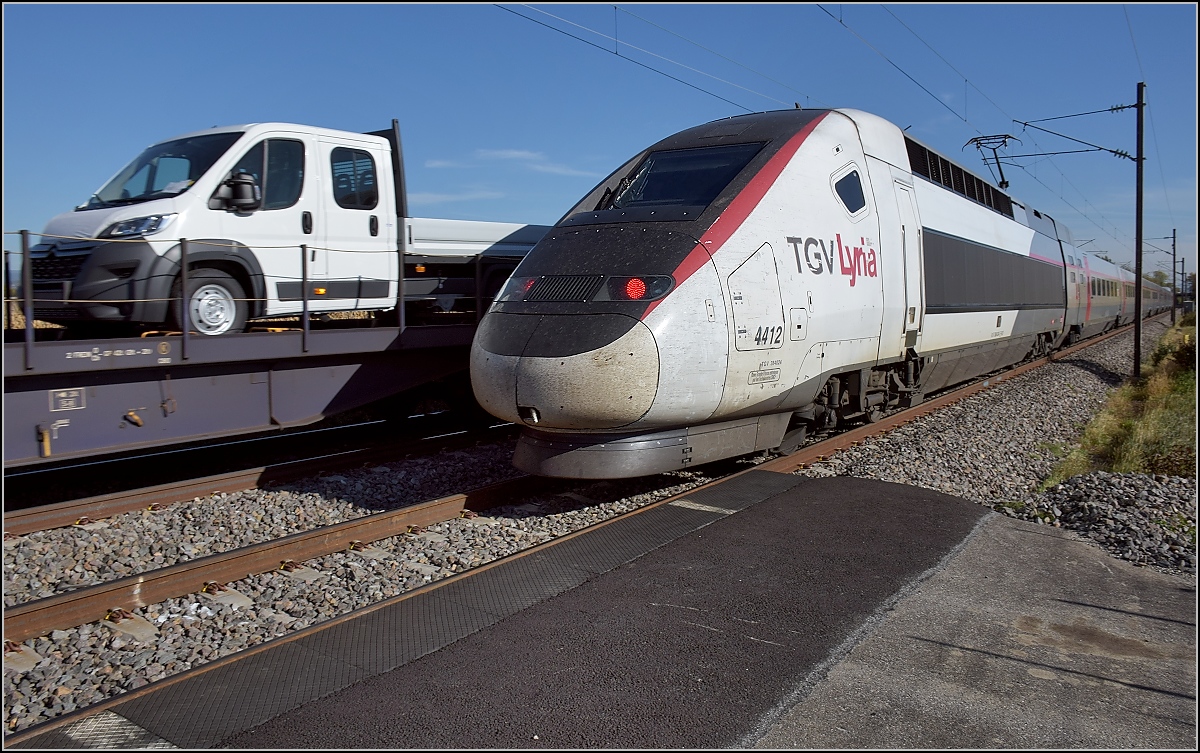 Bahn im südlichen Elsass. Etwas ungewöhnliche Begegnung von TGV Lyria 4412 mit dem schiebenden Triebkopf 384 024 und einem Kleintransporter. Bartenheim, Oktober 2017.