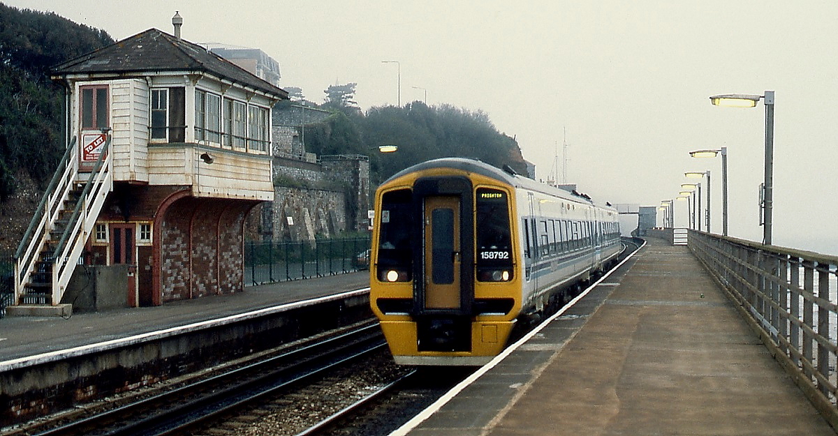 Bei typisch britischem Wetter fährt Class 158 792 im April 1992 in Dawlish ein. Das Stellwerk stand gerade zum Verkauf, vielleicht hat es ein Eisenbahnfreund mit dem notwendigen Kleingeld erworben.