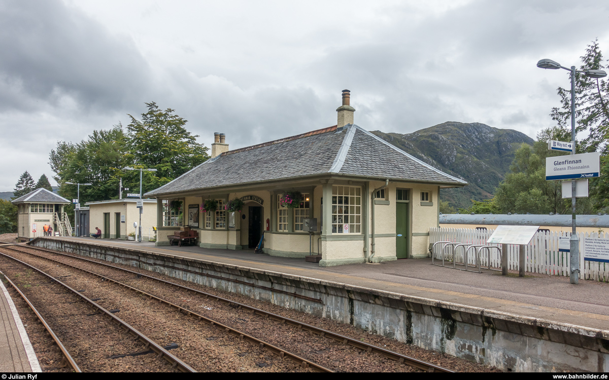 Der Bahnhof Glenfinnan am 25. August 2017. Das Bahnhofsgebäude beherbergt ein kleines Eisenbahnmuseum zur Geschichte der West Highland Line. Auch das Stellwerkhäuschen im Hintergrund kann besichtigt werden. Wie in weiten Teilen Schottlands üblich, ist auch der Bahnhof Glenfinnan zusätzlich in Gälischer Sprache angeschrieben.