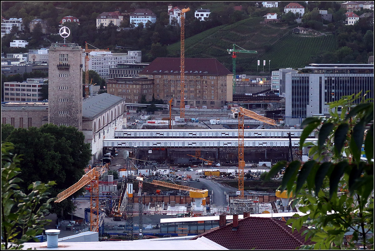 Die Bahnhofsbaustelle -

Blick von der Uhlandshöhe auf die Baugrube des neuen Stuttgarter Hauptbahnhofes. Laut Projektwebsite wird es ein Bahnhof der kurzen Wege, unter anderem auch deshalb weil er nur noch halb so breit wird als der alte.

Fast genau vor zwei Jahren sah die Baustelle aus der selben Perspektive so aus:
http://www.bahnbilder.de/bild/deutschland~bahnhoefe-r---z~stuttgart-hbf/890757/-die-bahnhofsbaugrube--quer-zu-den.html
Damals wurde in der Hauptsache noch die Baugrube freigemacht und ausgehoben. Die Fahrgastbrücken führten noch über stehengebliebene Bahnsteige, während sie heute an etwas anderen Positionen wirklich über Brücken führen. Im unteren Bildteil sind heute schon die ersten Abschnitte der Bahnsteige mit zwei Kelchstützenfüße (oben gelb verpackt) zu erkennen. Das ehemalige Bahndirektionsgebäude hinten in Bildmitte, steht jetzt zum Großteil auf Stützen um darunter den Tunnel bauen zu können.

19.08.2017 (M)