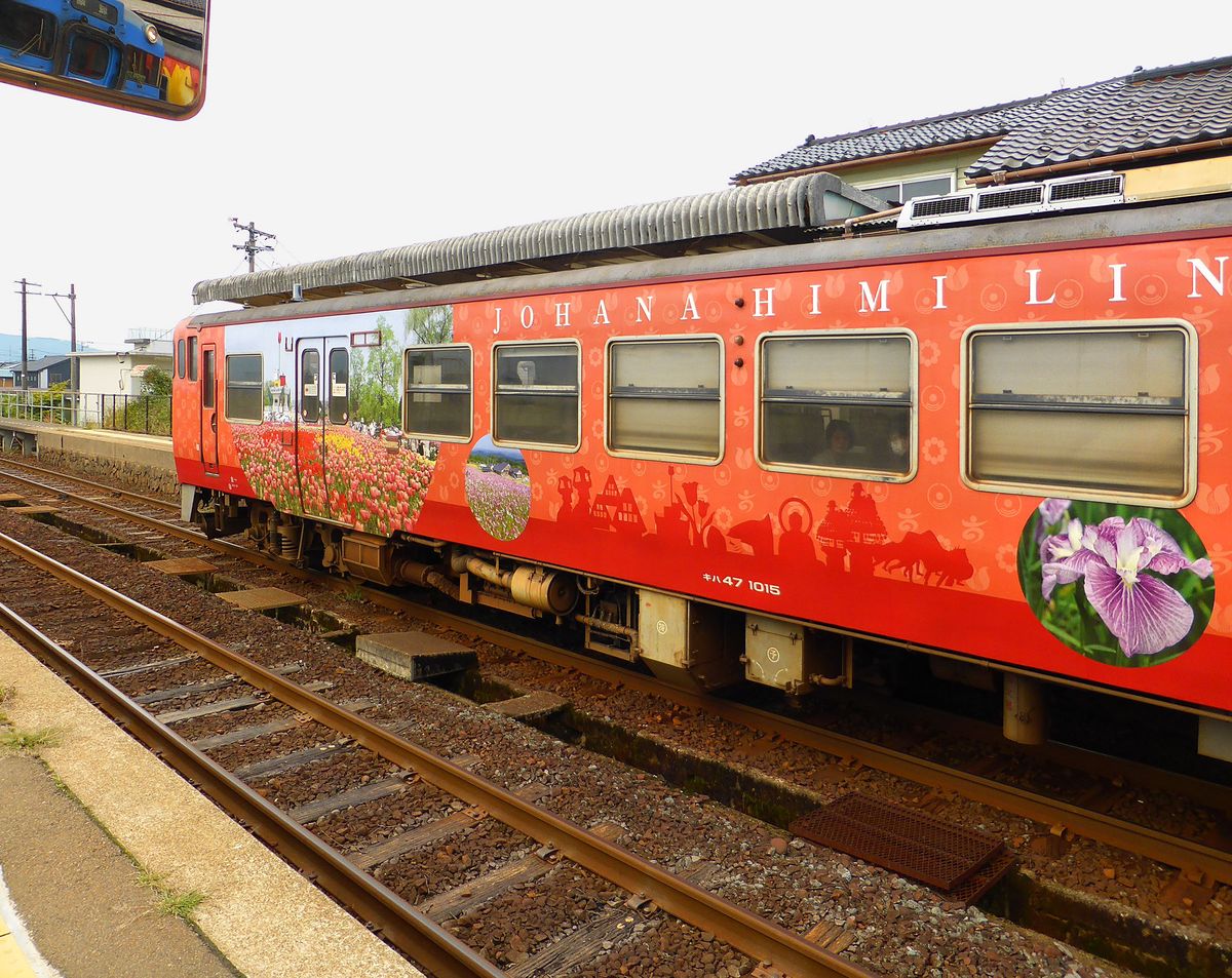 Die bunten Triebwagen der Region Takaoka: Die Jô-Hana-Linie führt ab Takaoka am Japanischen Meer ins Landesinnere nach Jô-Hana, von wo eine Busverbindung in die entlegensten Dörfer Zentraljapans besteht; in diesen Dörfern hat uraltes Kulturgut überlebt. Ich kann am Triebwagen KIHA 47 1015 im Mittelbild von links erkennen: ein Tanz der Reispflanzerinnen mit ihrem charakteristischen Spitzhut, alte Bauernhäuser, von rechts: ein Löwentanz (mehrere Tänzer unter einem stilisierten Löwen), riesige Wagen, auf denen die lokalen Gottheiten durchs Dorf gezogen werden, und eine Buddhastatue. Fukuno, 23.Oktober 2013. 