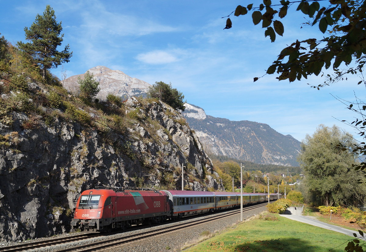 Die noch mit der Italien-Flagge versehene 1216 016 / E 190 016 zieht ihren EC 89  DB-ÖBB EuroCity  (München Hbf - Bologna Centrale) kurz vor dem Bahnhof Jenbach an der Wiesinger Steinwand vorbei durch die herbstliche Landschaft, 26.10.2018.