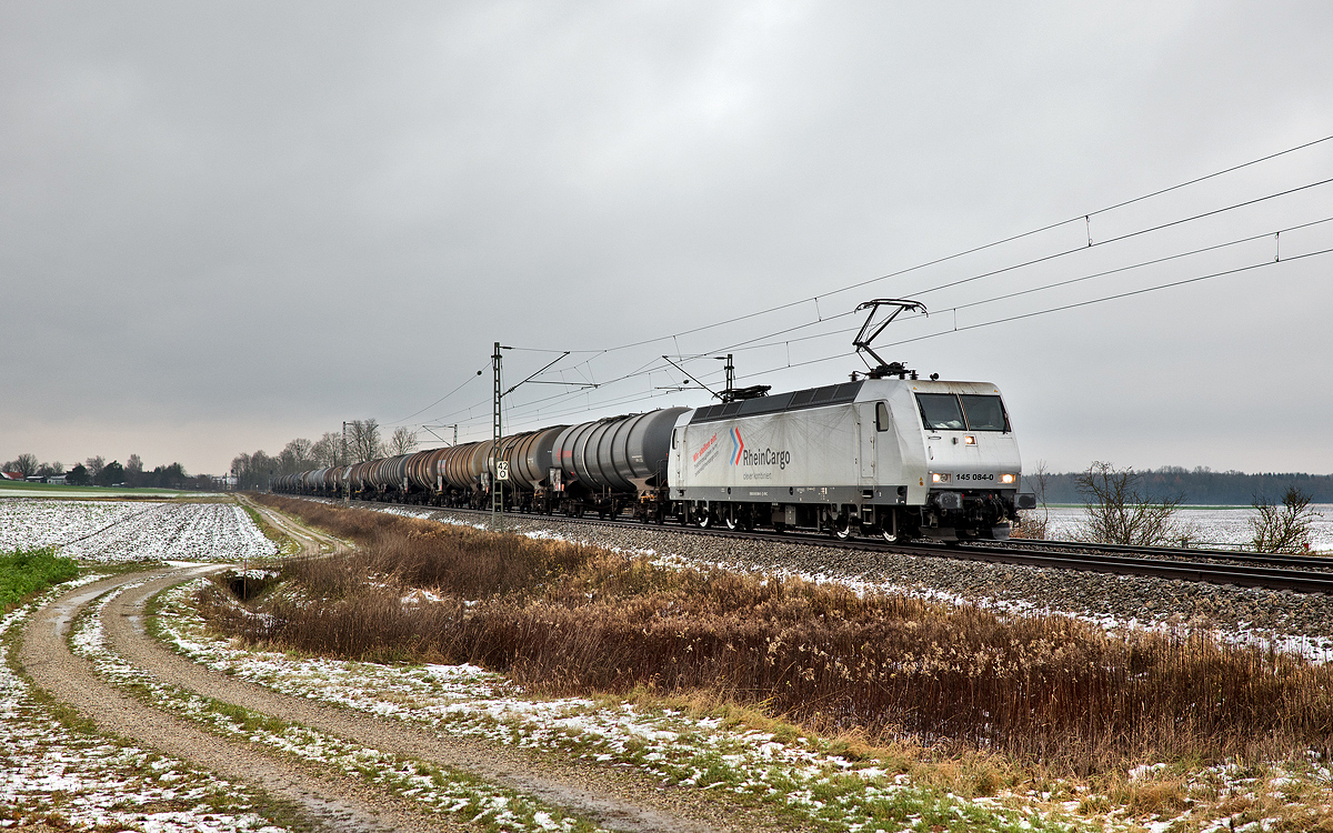 Die Rheincargo 145 084-0 fährt an einem trüben Tag in Langenisarhofen mit einem Kesselwagenzug nach Süden.Bild 5.12.2017