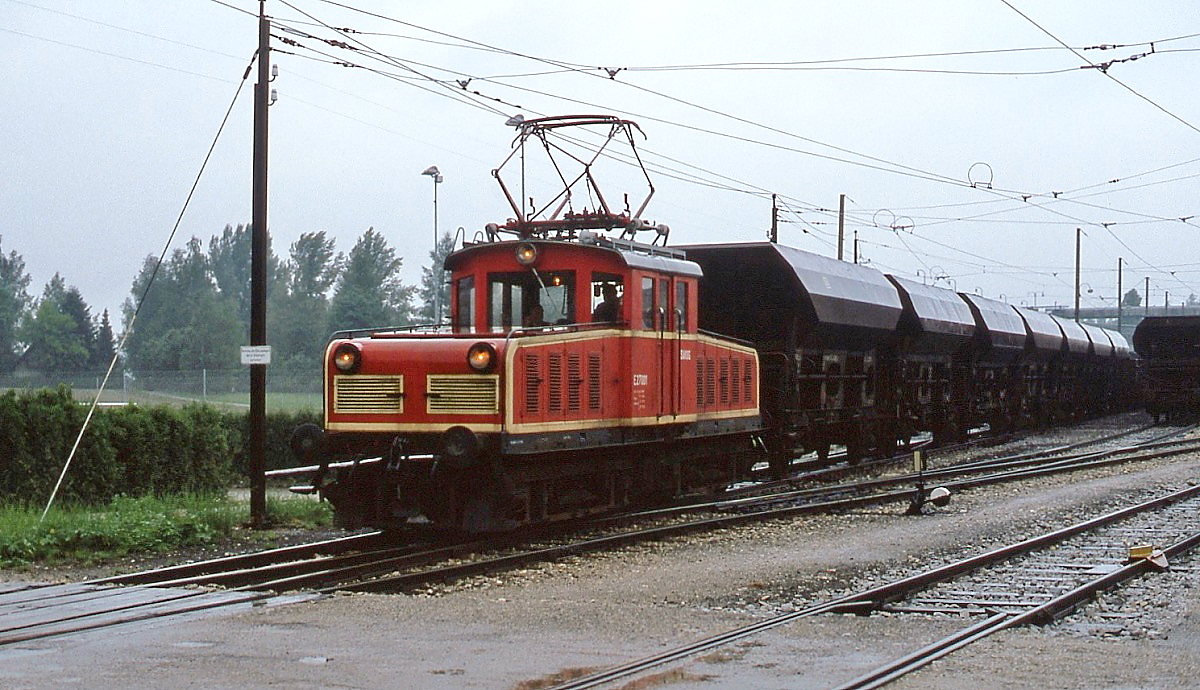Die im Stern & Hafferl-Nummernschema als E 27.001 eingereihte Bo'Bo'-Lok der Salzach-Kohlen-Bergbau-Gesellschaft (SAKOG) verlässt im Sommer 1980 mit einem Kohlezug den Bahnhof Trimelkam. Nach der Aufgabe des Kohlebergbaus 1993 wurde sie an die Salzburger Lokalbahn verkauft und dort als E 64 eingesetzt. 2019 kaufte Stern & Hafferl die Lok zurück. Die Strecke nach Bürmoos diente bis 1993 in erster Linie dem Abtransport der Kohle, der Personenverkehr spielte eher eine marginale Rolle.