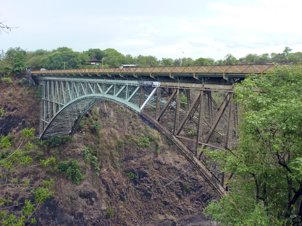 Die Victoria Falls Bridge stellt seit 1905 die Eisenbahnverbindung zwischen den heutigen Ländern Sambia und Simbabwe sicher. Seit 1929 dient die Brücke auch dem Straßenverkehr. An Bedeutung hat die Brücke seitdem nicht eingebüßt, ist es doch die einzige feste Querung des Sambesi im Abstand von hunderten Kilometern. Heutzutage ist die Brücke zudem eine Touristenattraktion und weltberühmter Bungee-Jumping Standort. Wer genau hinschaut erkennt in diesem Bild eine unter der Brücke hängende Person. Aufgenommen am 12.12.2014.