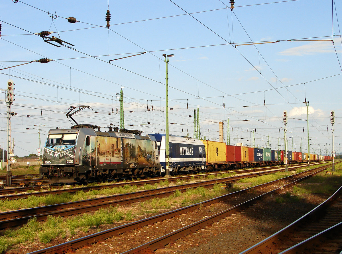 Die wunderschöne Werbelok von Metrans mit einem Containerzug von Budapest in Komárom Fbf. 386 020 mit Werbung  150 Jahre Hafenbahn Hamburg  (Eurorunner ist 761 003 von Metrans).
Komárom, 07.09.2017.