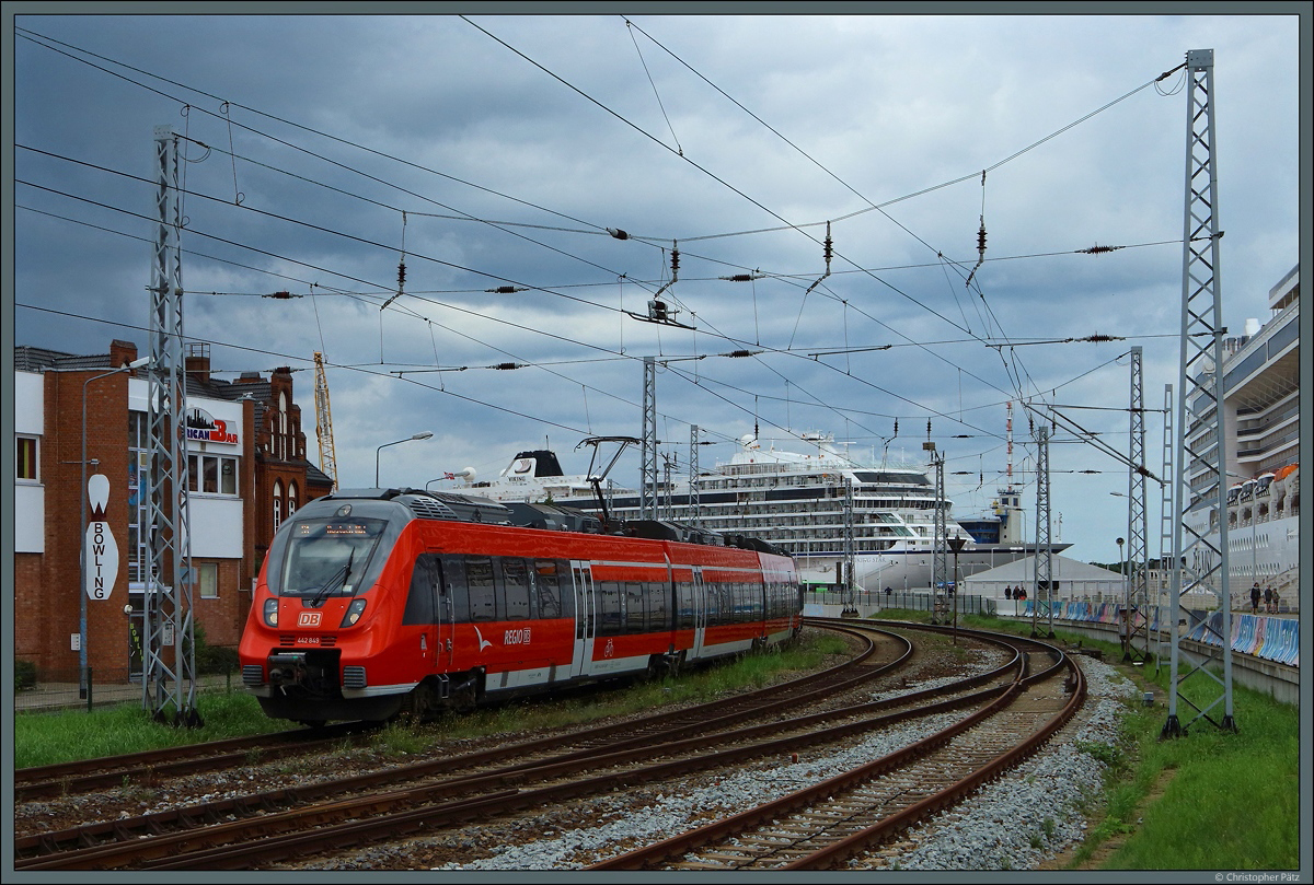 Dunkle Wolken brauen sich am Himmel zusammen, während 442 849 am 20.08.2017 dem Bahnhof Warnemünde verlässt. Dabei passiert der als S1 nach Rostock Hbf verkehrende Triebwagen das Kreuzfahrtschiff Viking Star.