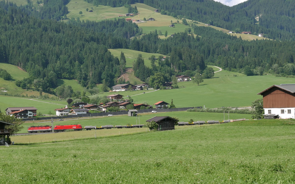 Eine 1144 und ein Taurus vor einem Zug mit Gleismaterial auf der Giselabahn zwischen Kitzbühel und Wörgl; Brixen im Thale, 12.06.2017
