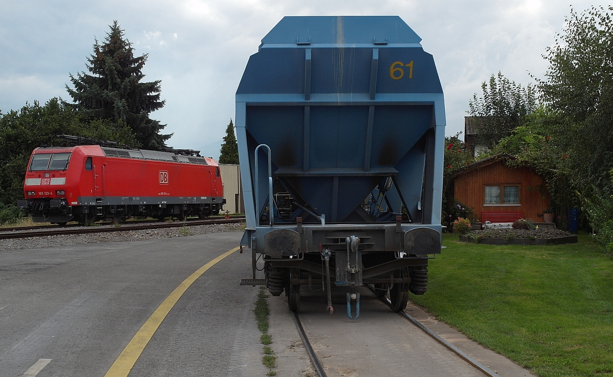 Eine E-Lok ohne Strom - ein abgekuppelter Schüttgutwagen - ein Gartenhäuschen. So gesehen am 24.08.2015 im Gewerbe-/Industriegebiet von Widnau (SG). 185 129-4 und Wagen vom Typ Fallns wurden vom Gehweg der Nöllenstraße aus fotografiert.