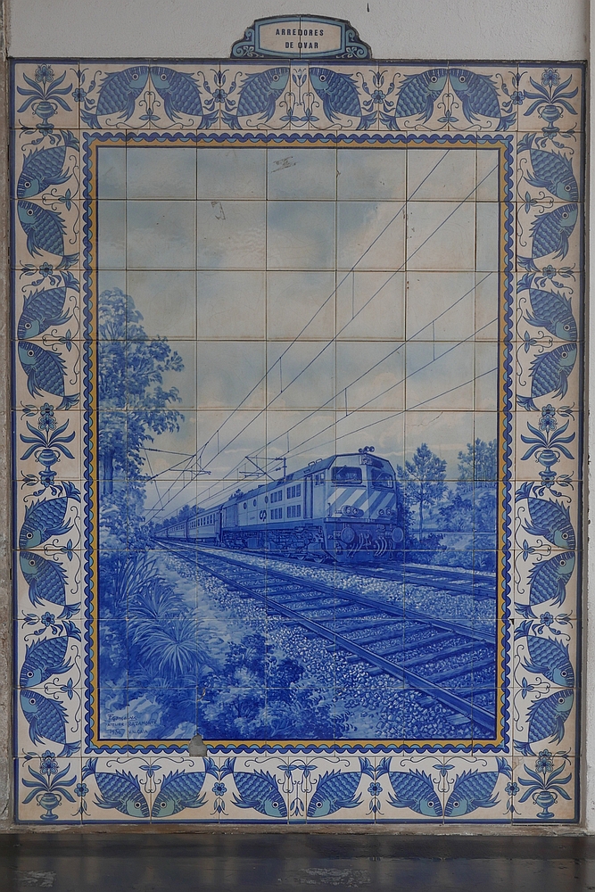 Eine Wandseite des Bahnhofgebäudes von Ovar ist mit mehreren Bildern, die aus bemalten Keramikfliesen hergestellt wurden, sogenannten Azulejos verziert. Ein Azulejo zeigt einen Personenzug, der von einer Diesellok der Baureihe 1960 durch das Umland von Ovar gezogen wird (11.10.2017).