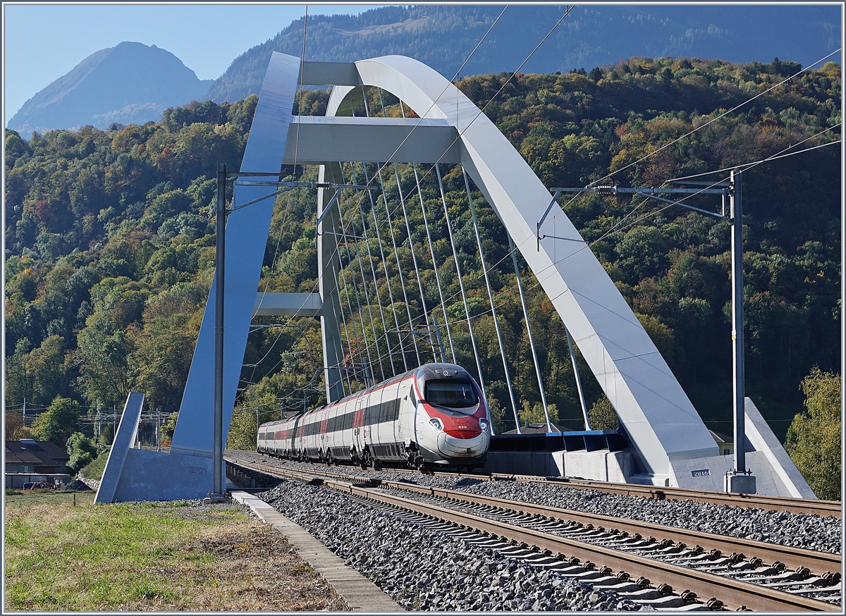 Fast 23 Meter über die Gleise wölben sich die beiden Bögen der SBB Brücke  Massongex , die zwischen Bex und St-Maurice über die Rhone führt. Die Brücke weist eine Spannweite von 125.8 Meter auf und gilt als längste Stählerne Eisenbahnbrücke der Schweiz. Sie ersetzt seit 2016 die beiden aus den Jahren 1903 und 1924 stammenden eingeleisigen Stahlbrücken. (Tech. Ang. Quelle: TEC21 Nr 41). 
Das Bild zeigt einen SBB ETR 610 der Als EC 32 von Milano nach Genève unterwegs ist.
 11. Okt. 2017 
