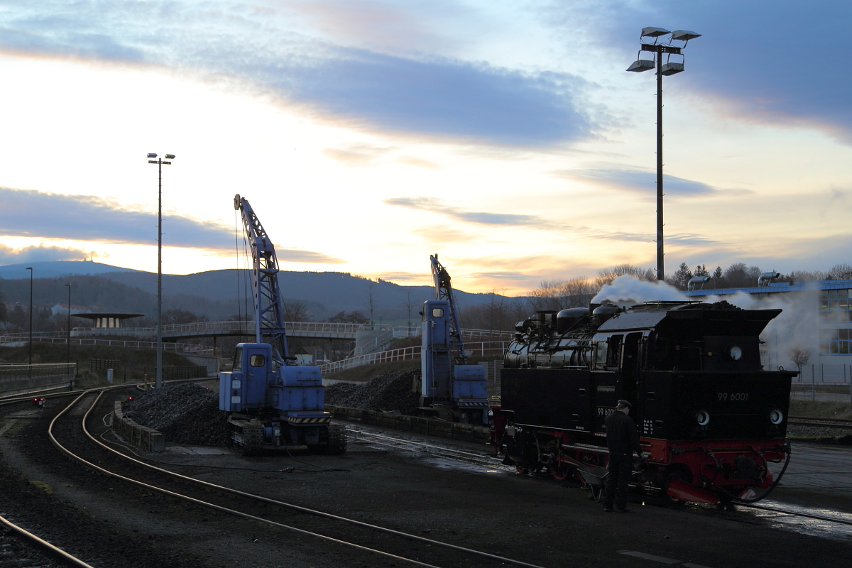 Feierabendstimmung am frühen Abend des 06.02.2016 an der Lokeinsatzstelle des Bahnwerkes Wernigerode. Während hinter dem Brocken die Sonne gerade untergegangen ist, wird an der Bekohlungsanlage Dampflok 99 6001 nach einem Sonderzugeinsatz für die IG HSB für die Entaschung vorbereitet.