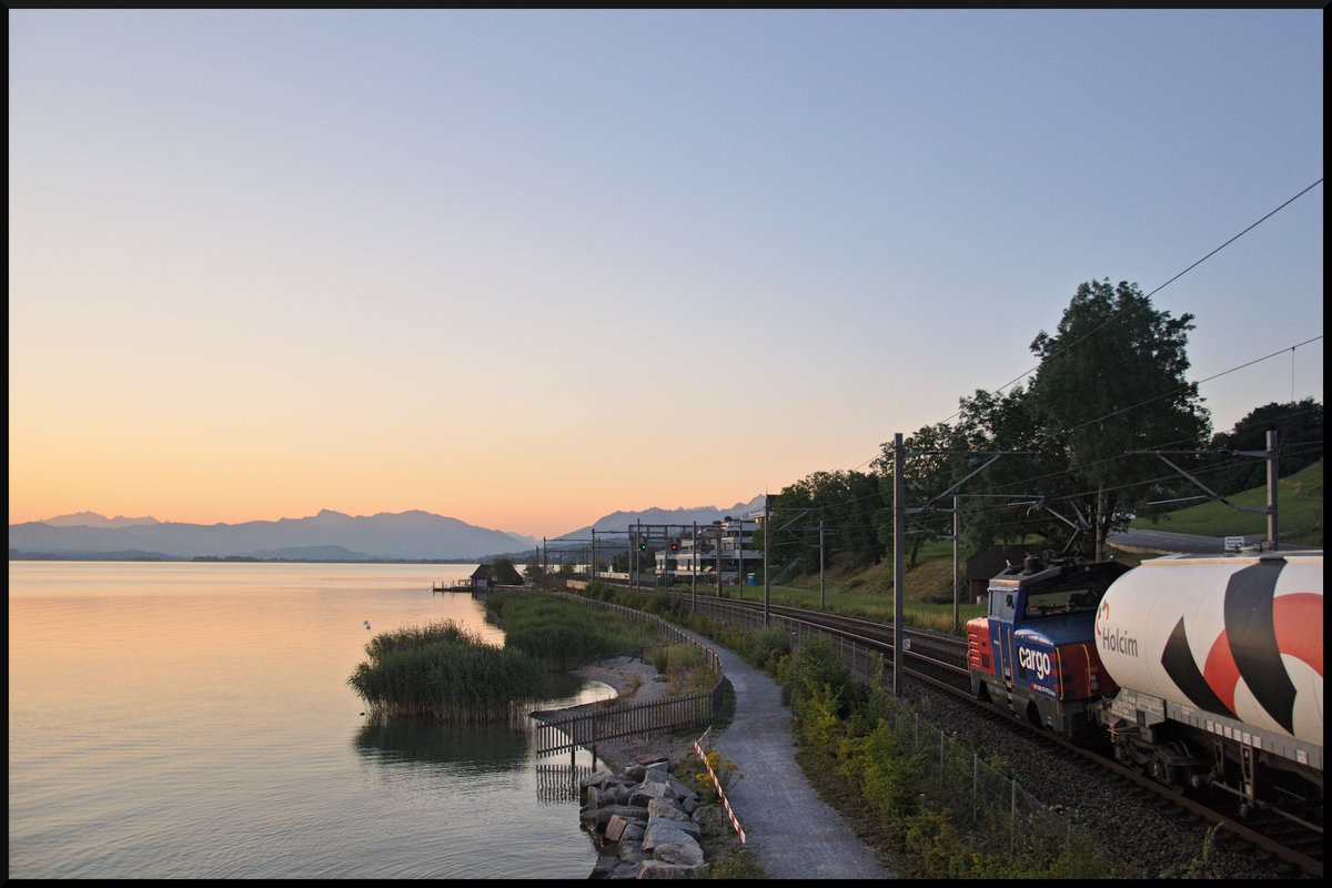 Frühmorgens am Ufer des Zürichsees: Die Eem 923 026-9  Hofberg  befindet sich mit wenigen Güterwagen auf dem Weg in Richtung Pfäffikon SZ. Aufgenommen zwischen Wädenswil und Richterswil am 06.07.2017