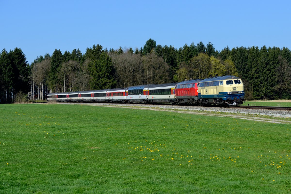 In den ersten Monaten des Jahres 2017 verbrachte die 218 460 der Westfrankenbahn einige Zeit bei der Südostbayernbahn in Mühldorf, um den dortigen Lokmangel zu lindern. Zumeist war sie vor Regionalzügen auf der KBS 940 unterwegs. Anfang April gab es jedoch ein paar Einsätze im EC-Verkehr von und nach Lindau. Die vorbildlich restaurierte Lok in der Ursprungsfarbgebung ozeanblau-beige löste eine ziemliche Hysterie unter Eisenbahnfreunden aus und bewegte manch einen von ihnen zu einer weiteren Anreise, um die Fahrten durch das Allgäu zu dokumentieren. Eigentlich erstaunlich, war diese Lackierung doch einst sehr unbeliebt bei den Fotografen. So ganz konnte ich mich dem Spektakel auch nicht entziehen und deswegen entstand am 09. April 2017 diese Aufnahme von 218 460 (Spitzname Conny) und ihrer Mühldorfer Schwester 218 421 vor dem EC 191 nach München HBF in den Wäldern bei Ungerhausen im Unterallgäu.  