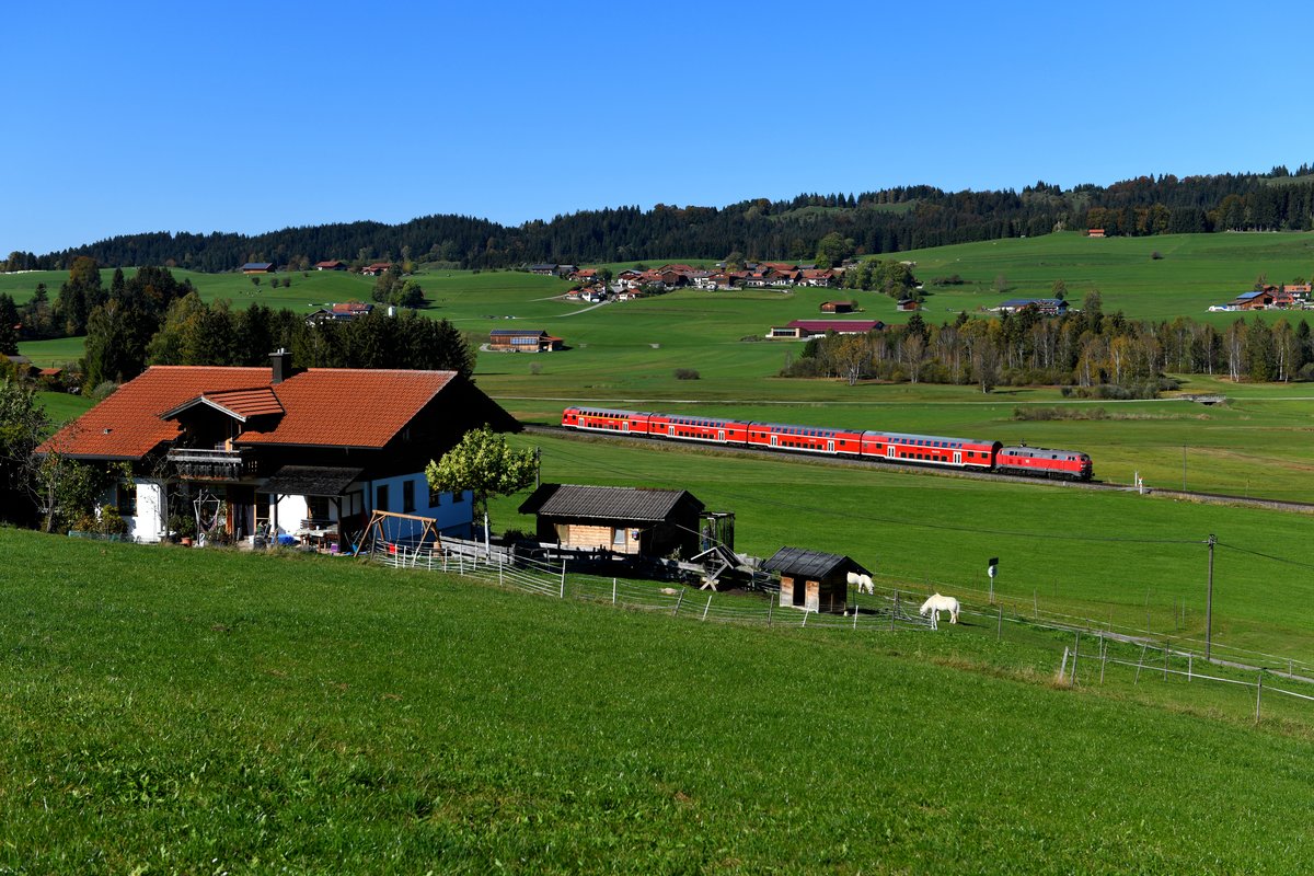 In der Gegend von Hopferau ergeben sich einige Fotomotive, so auch dieser idyllische Blick auf den kleinen Weiler Heimen. Am 14. Oktober 2018 schob 218 411 den RE 57511 von Füssen nach München HBF und wird bald den ersten Haltepunkt Weizern-Hopferau erreichen. 