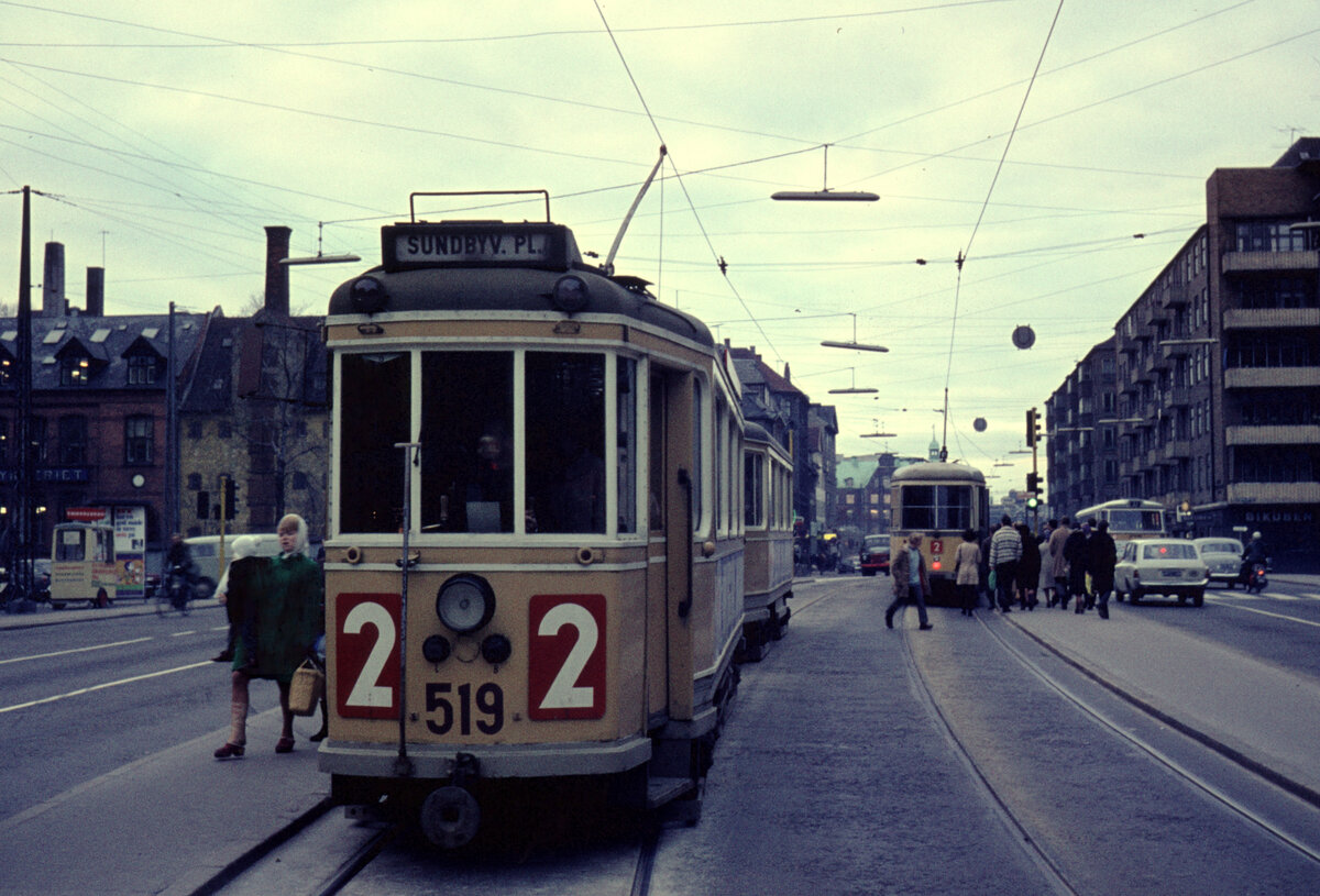 København / Kopenhagen Københavns Sporveje (KS) SL 2 (Großraumtriebwagen 519) København K, Christianshavn, Torvegade / Christianshavns Torv im November 1968. - Der Zug fährt bis Sundbyvester Plads auf der Insel Amager, während der DÜWAG/Kiepe-GT6, den man im Hintergrund sehen kann, auf dem Weg nach Brønshøj ist. - Auf dem Bürgersteig links im Hintergrund hält ein kleiner gelber Wagen; von solchen Wagen verkaufte man früher dänisches Smörrebröd (: belegtes Brot). - Scan eines Diapositivs. Kamera: Canon Canonet QL 28.