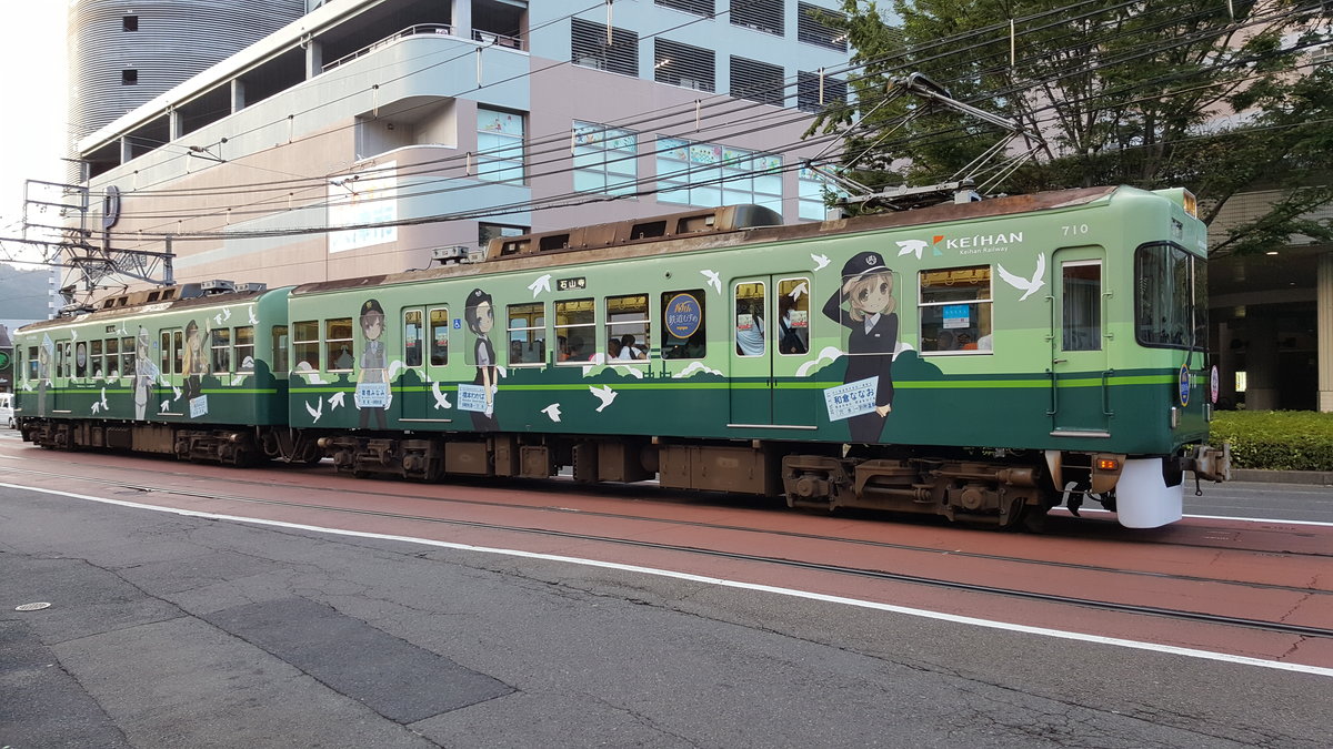 Keihan Serie 700 Wagen 709/710 wartet an der Kreuzung vor dem Bahnhof Hamaotsu auf Fahrt, 28.08.2016

Der Zug trägt das  Tetsudou Musume Tour 2015  Design. Tetusdou Musume ist ein Projekt der Privatbahnen in Japan, bei dem jede teilnehmenden Bahngesellschaft mindestens ein Maskottchen beisteuert.