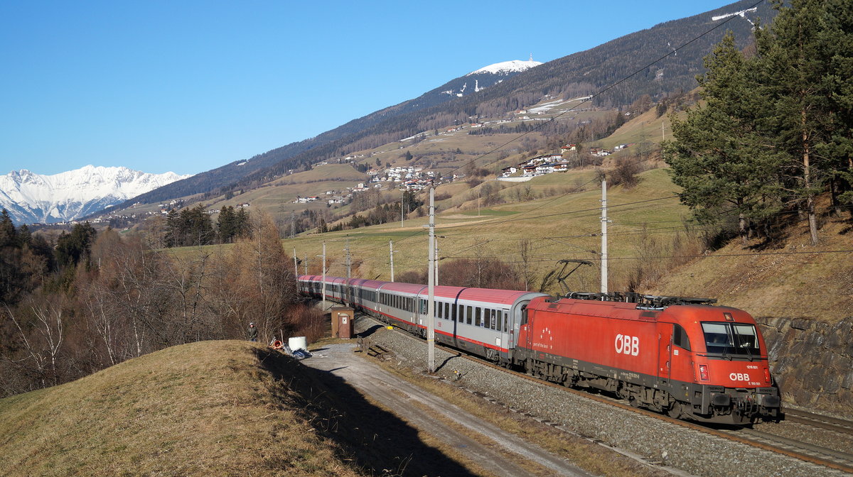 Klassisches Bahnflair bringen die DB-ÖBB Eurocity-Züge der Relation München - Italien mit sich. Hier ist die 1216 001 mit dem EC 87 nach Venezia Santa Lucia auf dem Weg Richtung Grenze am Brenner und fährt bei bestem Sonnenschein durch Mühlbachl, während im Hintergrund die verschneite Nordkette über Innsbruck zu erkennen ist. 29.12.2018.