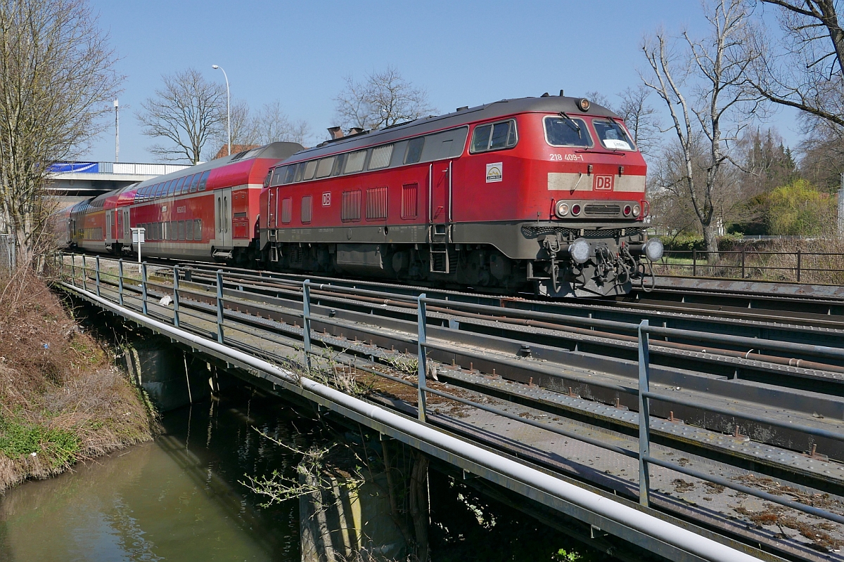 Kurz nach der Abfahrt in Biberach (Riß) zieht 218 409-1 die Wagen des IRE 4215, Stuttgart - Lindau über den Rotbach, der hinter der Brücke in die Riß fließt (28.03.2017).