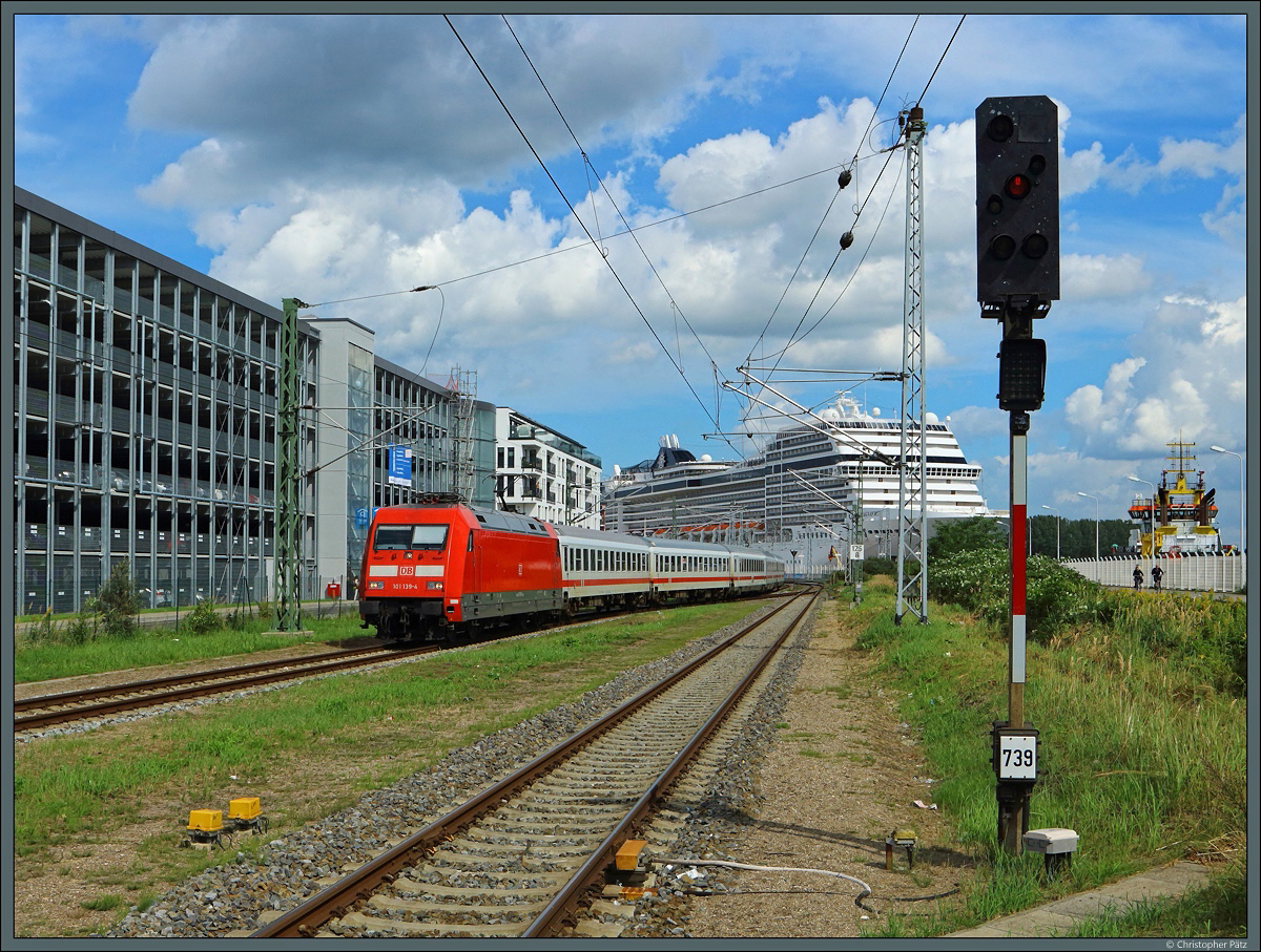 Mit dem IC 2239  Warnow  verlässt 101 139-4 am 20.08.2017 den Bahnhof Warnemünde. Im Hafen liegt gerade das Kreuzfahrtschiff MSC Magnifica vor Anker.