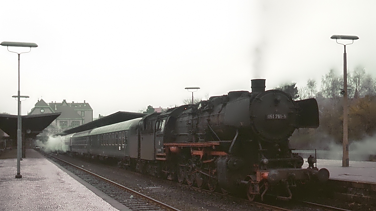 Mit dem Wechsel auf den Sommerfahrplan 1976 endete der planmäßige Einsatz von Dampflokomotiven vor Reisezügen bei der DB. Diese letzten Einsätze erbrachten Lokomotiven der Baureihen 044 des Bw Ottbergen und 050 des Bw Lehrte auf der Strecke von Bad Harzburg nach Goslar. Hier wartet die Lehrter 051 761-5 am 24.04.1976 im Bahnhof Bad Harzburg vor einem Eilzug auf die Ausfahrt nach Goslar. Zwar hatte sich der morgendliche dichte Nebel bereits etwas verzogen, die eigentlich von hier sichtbaren Harzberge versteckten sich aber weiterhin in den Wolken. Anscheinend war die Dampfheizung zwischen dem 3. und 4. Wagen des Zuges nicht ganz dicht.