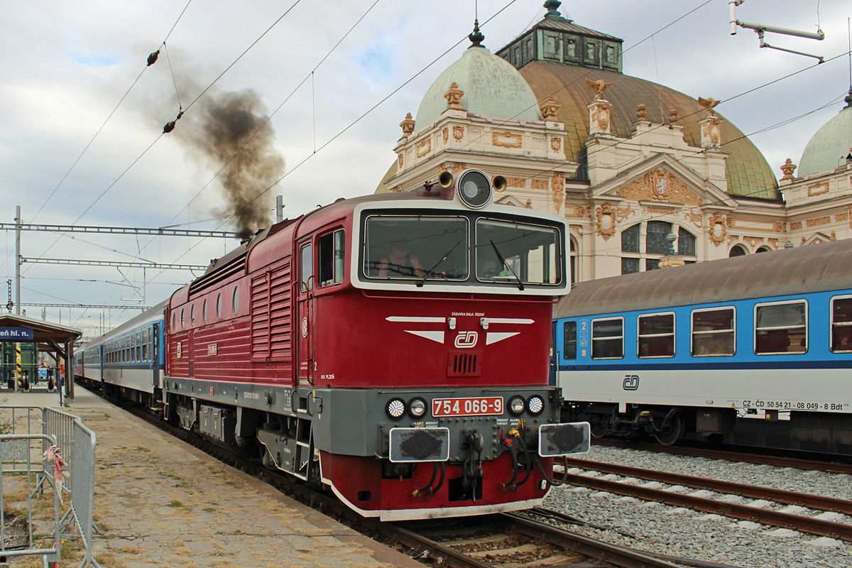 Nachdem alle Fahrgäste ausgestiegen sind, startet 754 066 wieder den Motor, um den Zug vom Bahnsteig wegzuziehen. Im Hintergrund das sehenswerte EMpfangsgebäude von Plzeň hl.n. am 14.09.2015