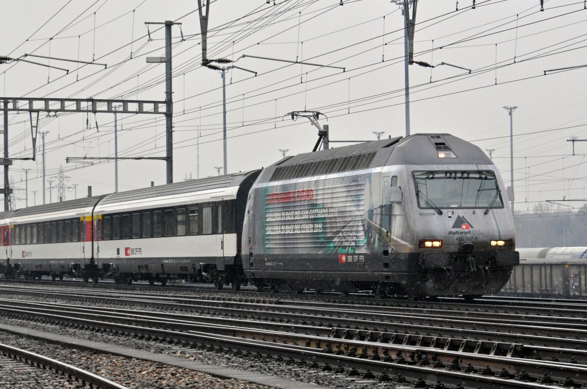 Re 460 107-6 mit der Gotthardtunnel Werbung durchfährt bei leichtem Schneefall den Bahnhof Muttenz. Die Aufnahme stammt vom 26.01.2015.